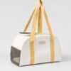 Cream soft pet carrier with yellow webbing handles and a grey mesh end panel on a plain background.