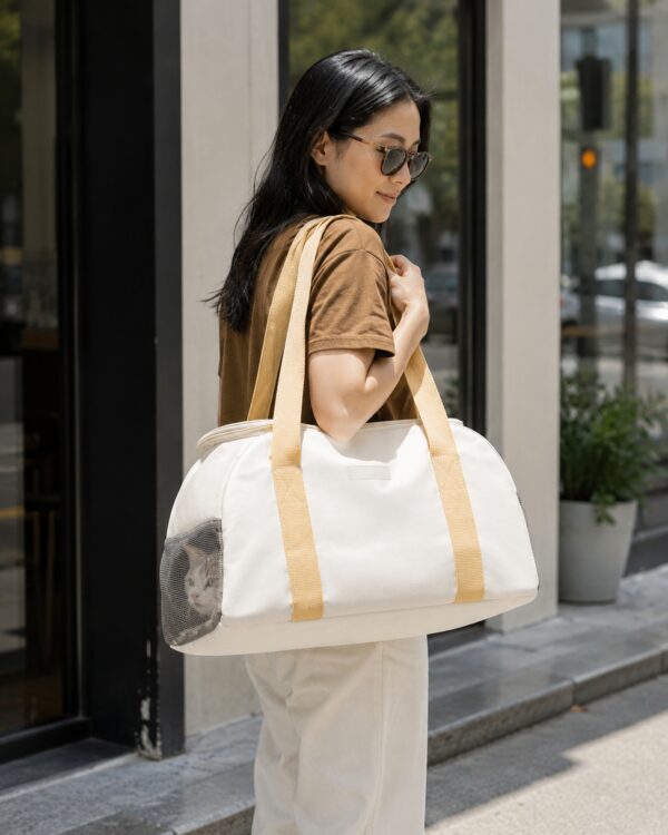A woman carries the cream and yellow pet carrier by its handles along a city street.