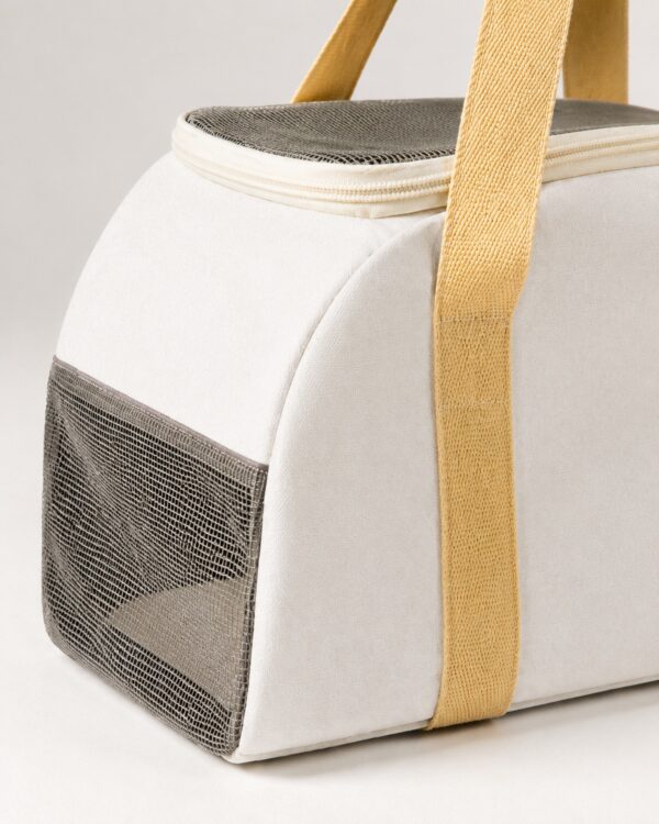 Close-up of the cream pet carrier showing its grey mesh side panel and yellow handles.