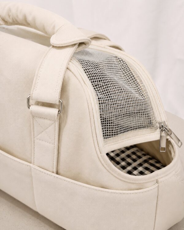Close-up of the cream pet tote showing its gingham lining and mesh side panel.