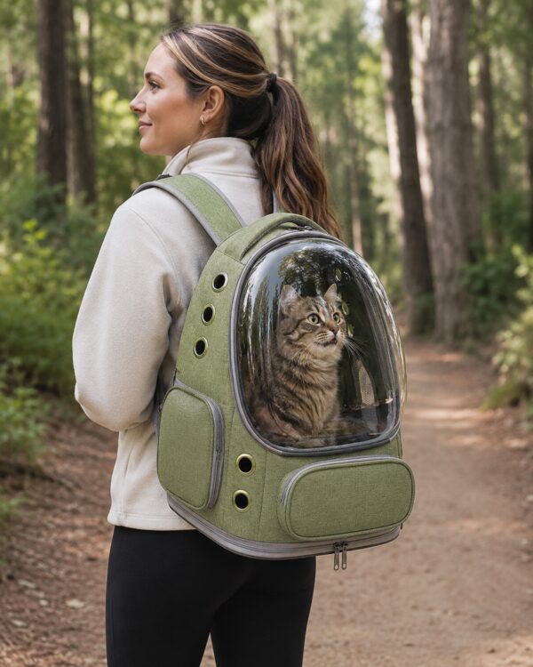 A woman carries the olive pet backpack on a trail with a tabby cat watching from the dome.