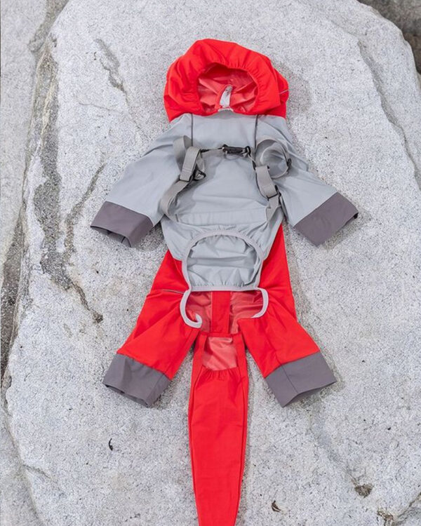 The red and grey rain suit laid on a rock showing its back zip and straps.