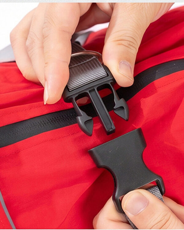 Hands fasten the black buckle on the red dog rain suit.