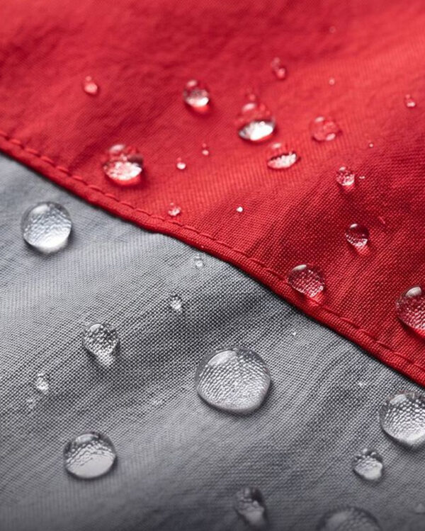 Close-up of water beading on the red and grey fabric of the dog rain suit.
