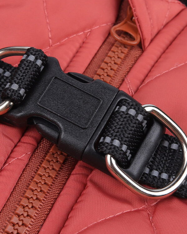 Close-up of the coat's black side-release buckle with a nickel D-ring on each side, over the brown back zip.