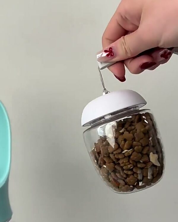 Clear food cup full of kibble with a white cap, lifted out of the bottle by its gray lanyard