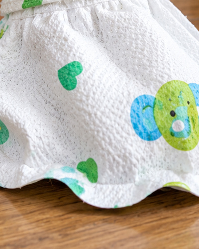 White textured fabric and an elephant print curve over a poodle’s covered paw.