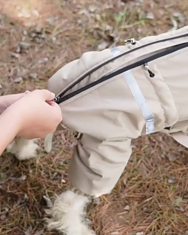 Hands open the back zipper of a khaki four-leg dog suit outdoors.